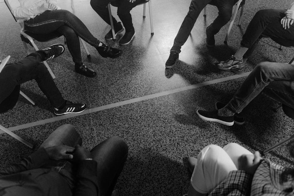 Black and white photo of a support group session indoors with diverse participants. Photo by Tima Miroshnichenko