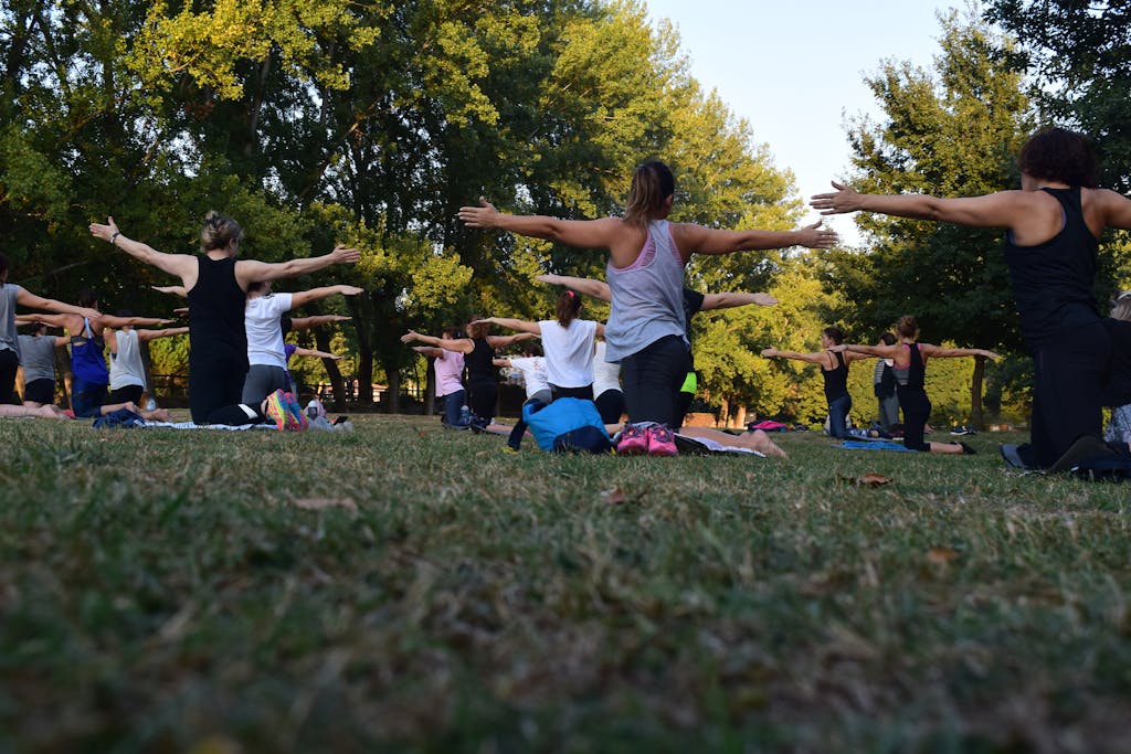 Group of adults practicing yoga outdoors in a park surrounded by trees.Photo by Rui Dias